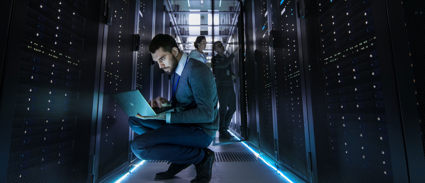 IT Technician Works on Laptop in Big Data Center full of Rack Servers. Multiple People Works at Data Center at the same time.