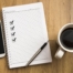 Note book with four check marks, smartphone, a pen and a cup of coffee on wooden background.
