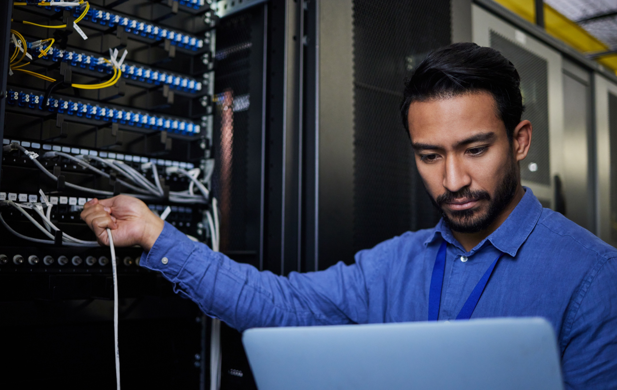 Engineer laptop, server room and cable connection for software update or maintenance at night. Cybersecurity coder, cloud computing and programmer man with computer for networking in data center.