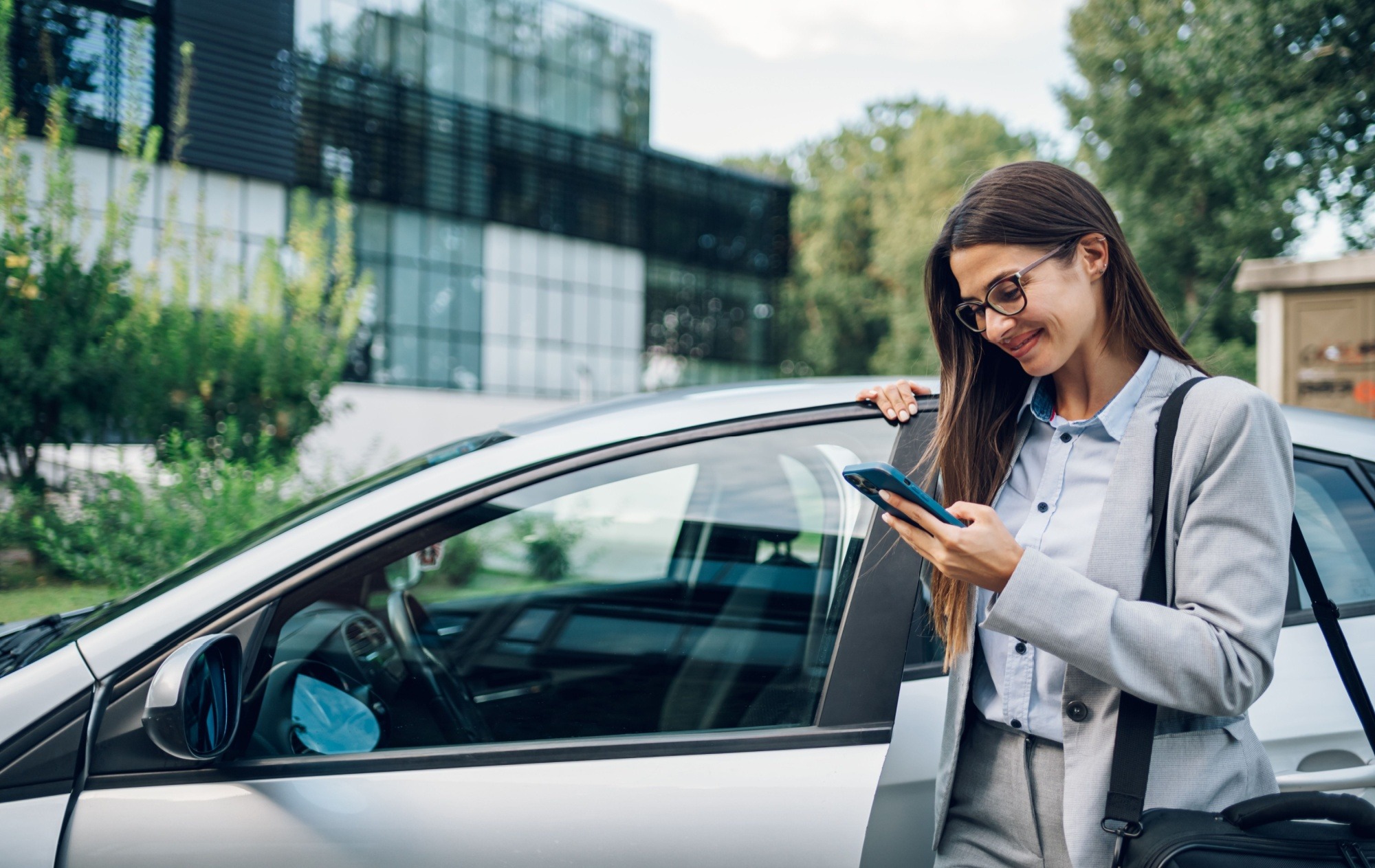 Businesswoman using mobile phone while standing next to open car door.