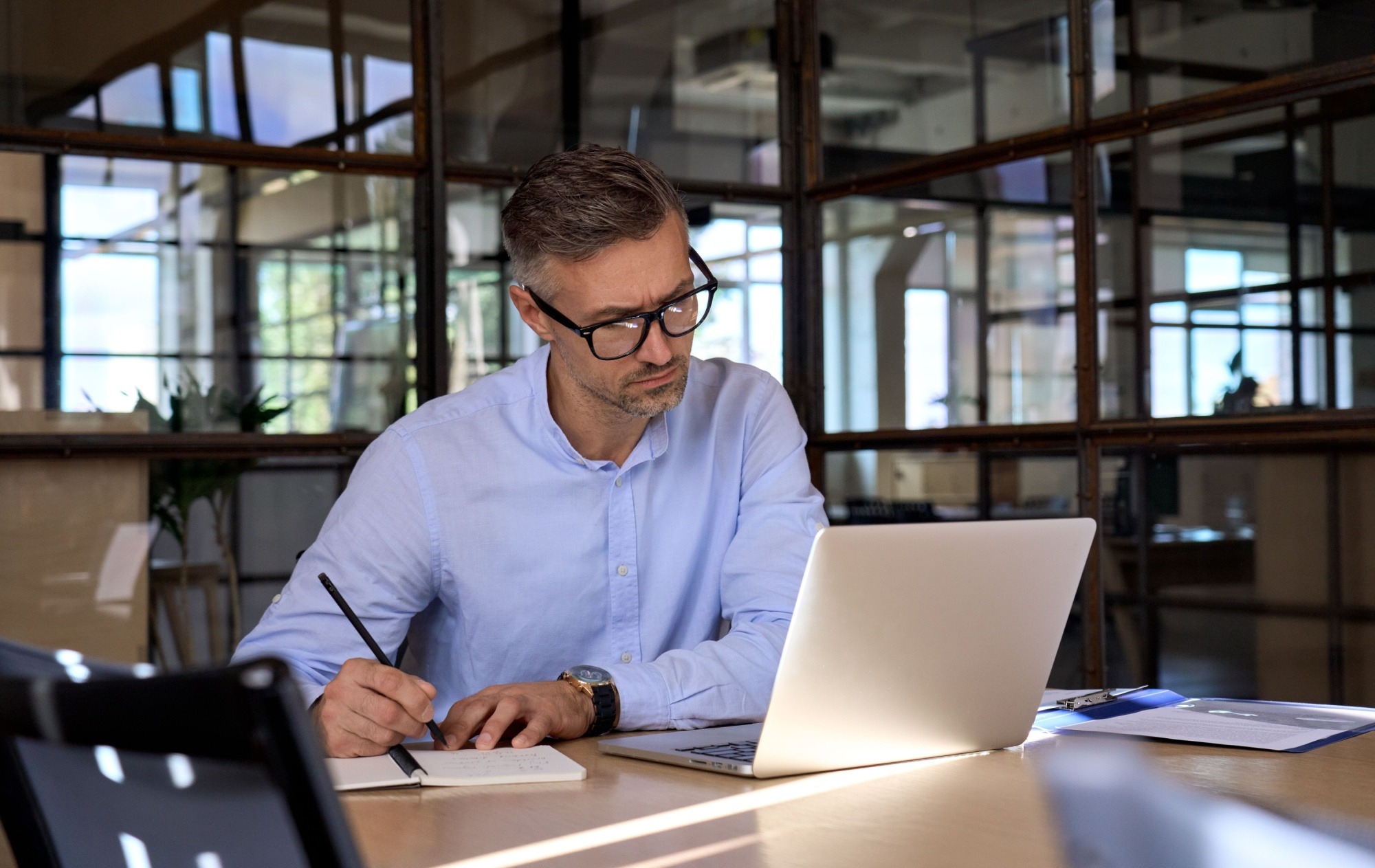 Mature business man executive manager looking at laptop computer having virtual meeting video conference taking notes, doing market research working in office.