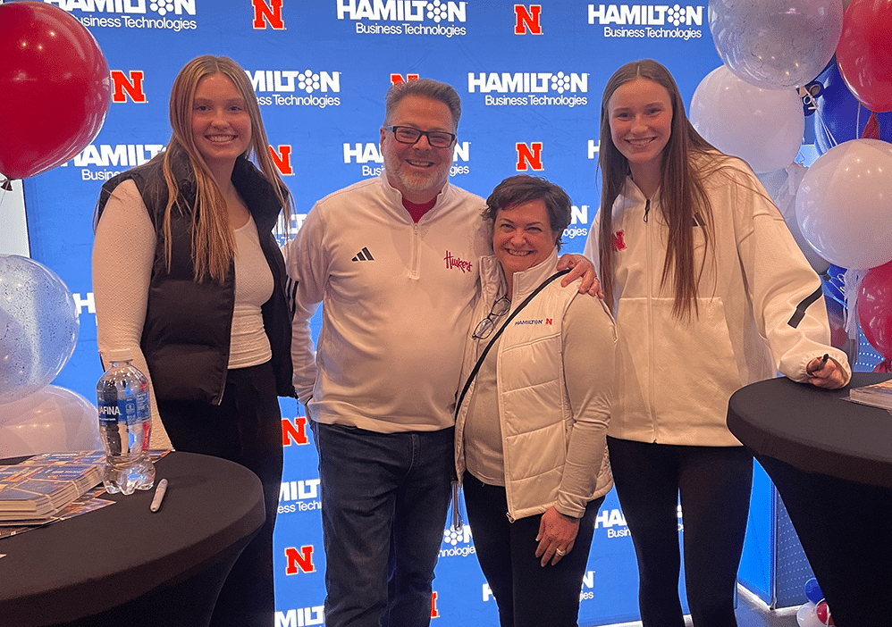 Hamilton CEO John Nelson and his wife standing with 2 Nebraska Volleyball players at an event